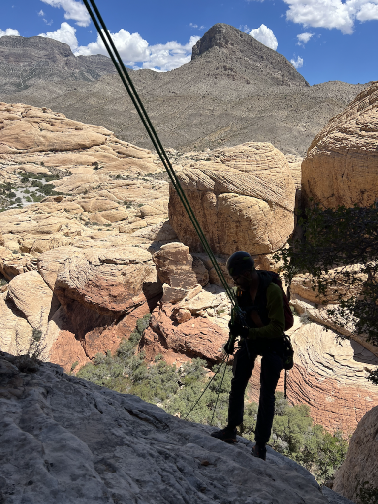 Climber rappelling down a cliff in a desert landscape.